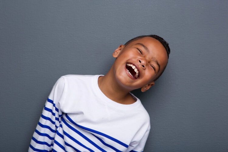 A cheerful young boy in a striped shirt bursts into laughter, exuding pure joy.